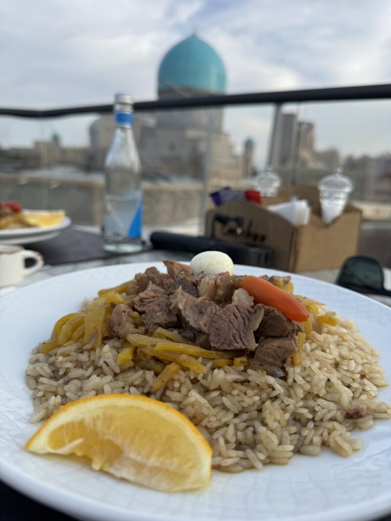 typické uzbecké jedlo plov pozostávajúce z mäsa a ryže v pozadí panoráma mesta Samarkand