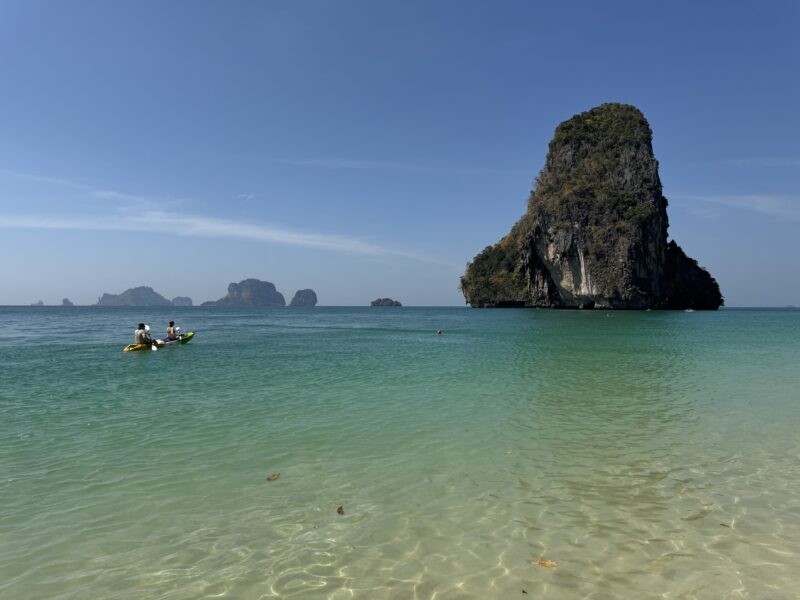 Phra Nang beach, Thajsko čo vedieť pred cestou do Juhovýchodnej Ázie - more a vápencová skala trčiaca z vody, turisti v kajaku plaviaci sa ku skale
